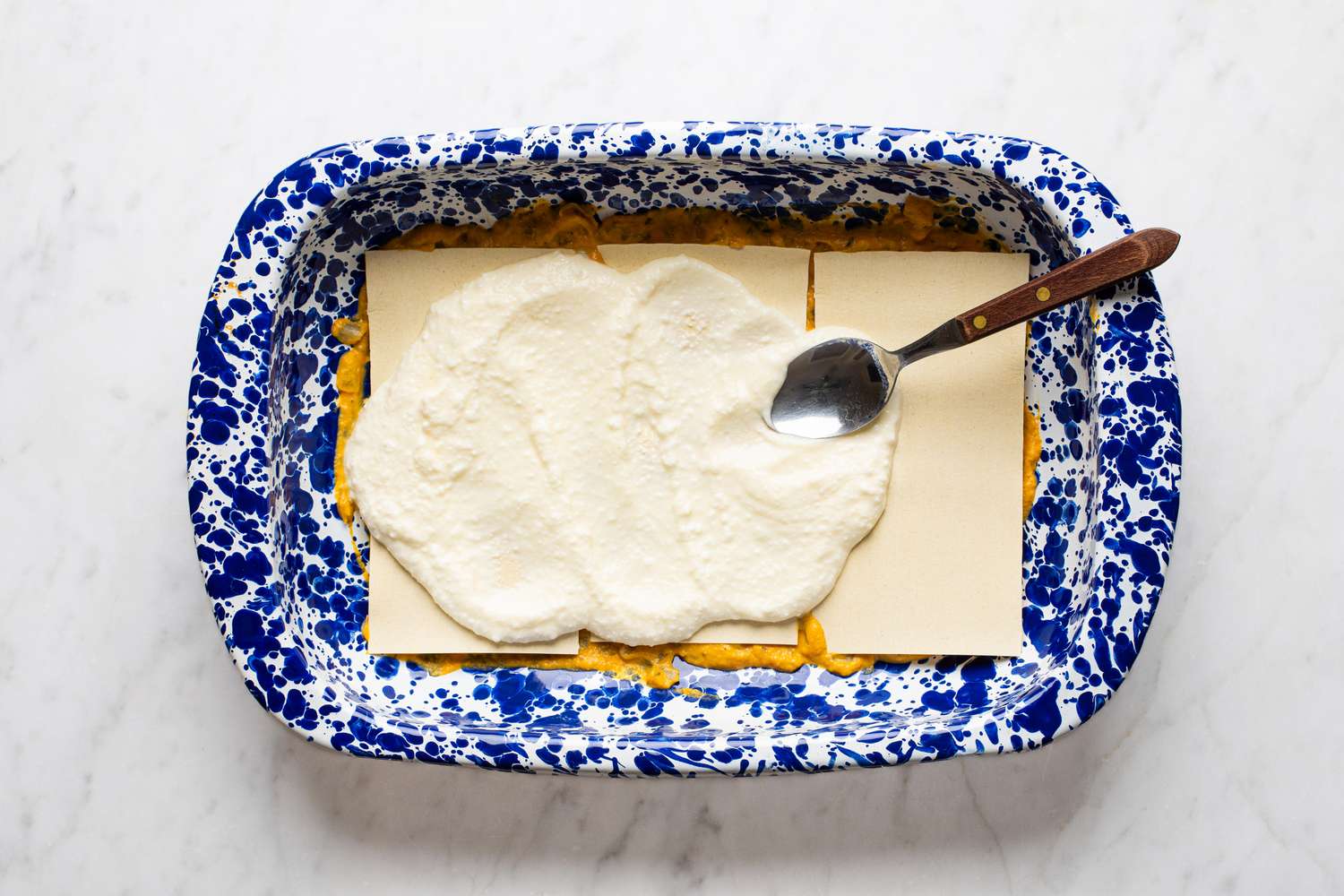 Overhead view of casserole dish with pumpkin mixture coating the bottom, lasagna noodles on top, and cheesy mixture on top of noodles for Easy Pumpkin Lasagna