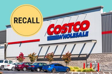 Costco storefront with a recall announcement badge above it parked cars in the foreground