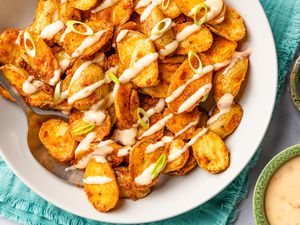 bang bang potatoes topped with sauce in a bowl at a table setting next to small bowl with more sauce and a bowl with sliced scallions