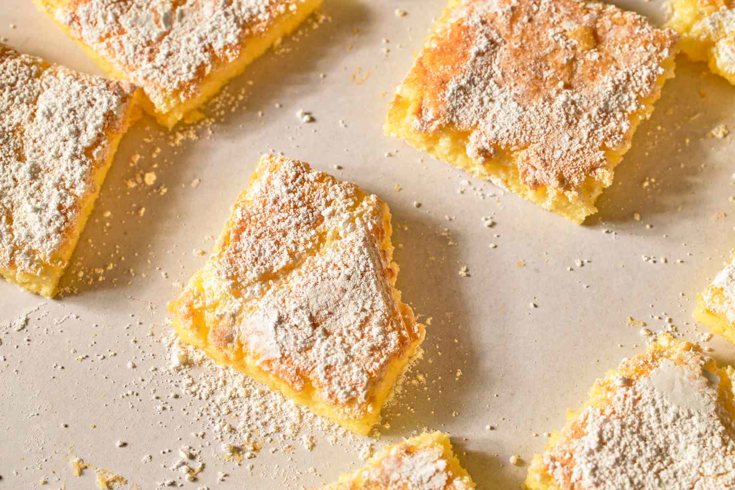 Square dessert bars dusted with powdered sugar on parchment paper