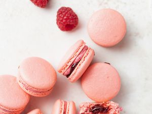 Overhead view of French macarons with raspberry buttercream filling and whole raspberries next to them.