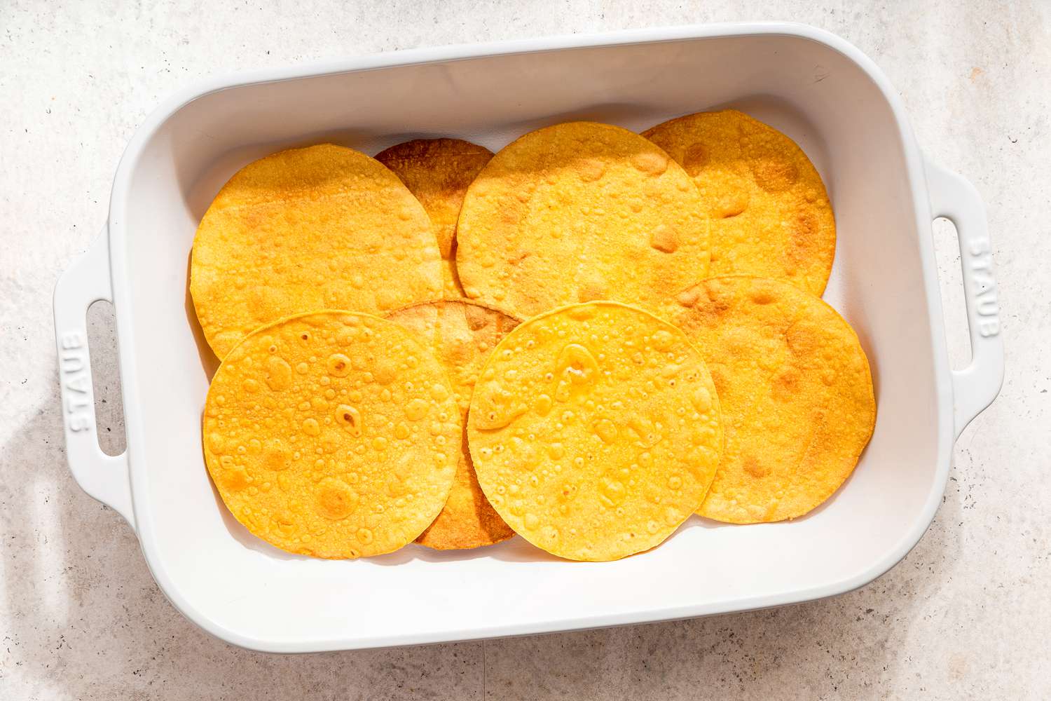 Assembling chicken taco casserole: tostadas on the bottom of a casserole dish 