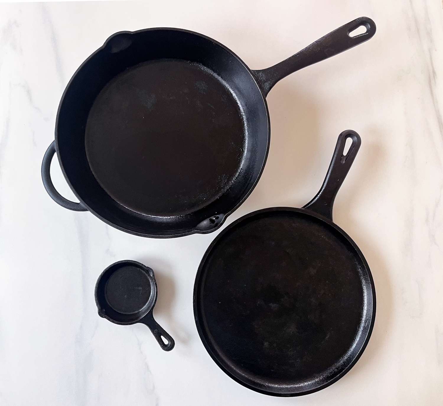 Three cast iron skillets of varying sizes placed on a light surface