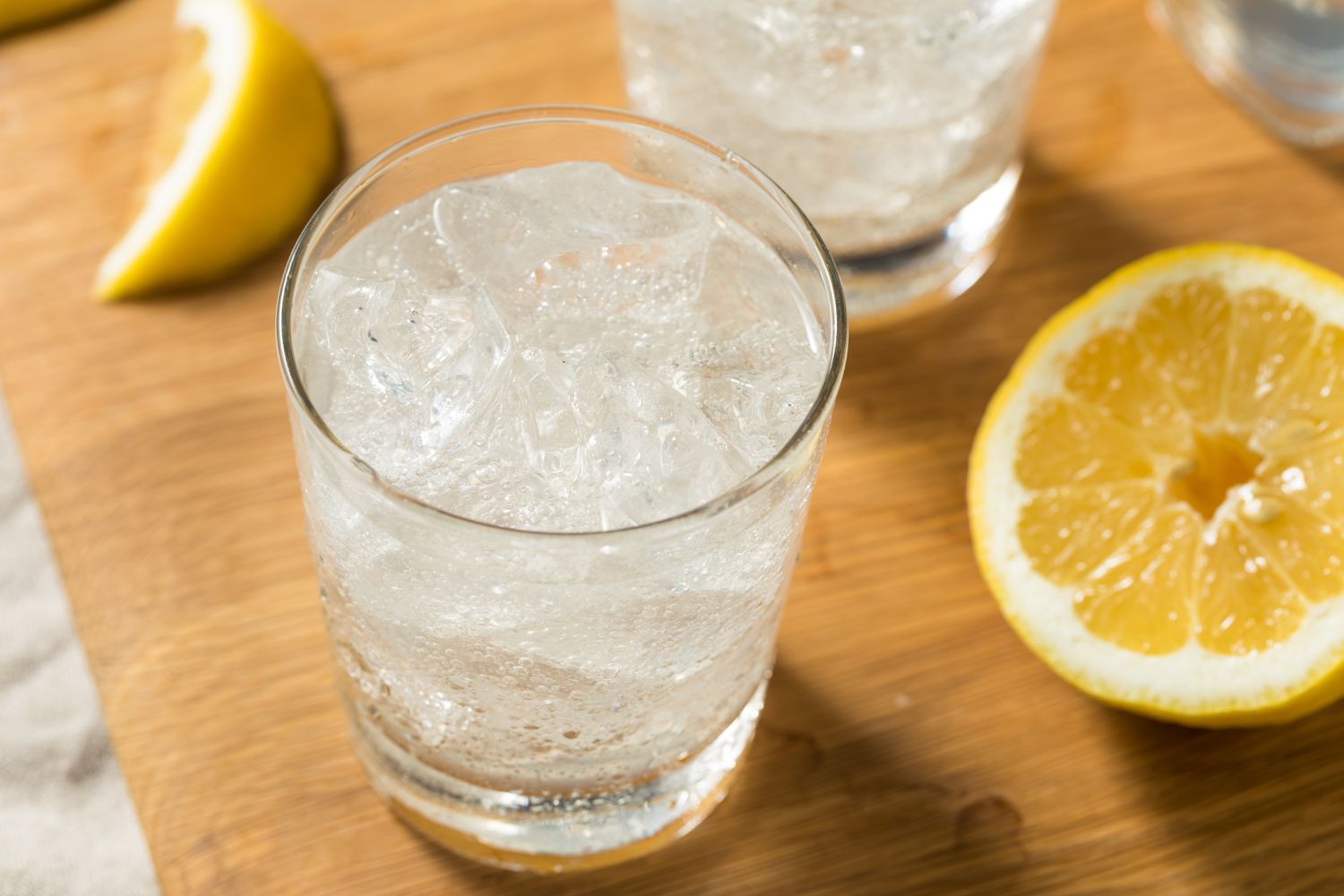 Angled view of a glass of sparkling water on a wooden cutting board next to lemon slices