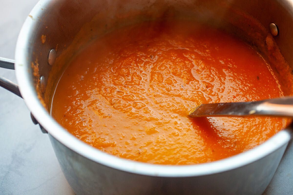 Carrot soup in a pot and a spoon in it, simmering