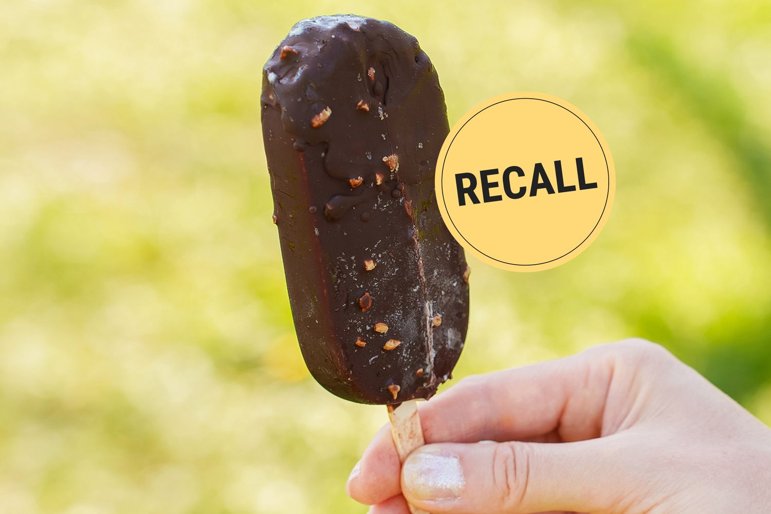 Hand holding a chocolatecovered ice cream bar next to a recall notice