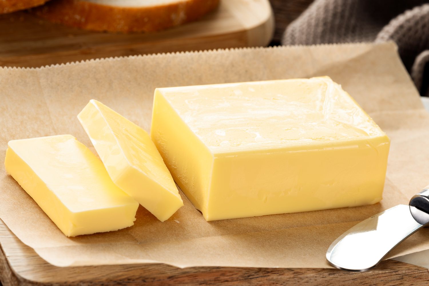 A stick of butter with slices arranged on parchment accompanied by a butter knife