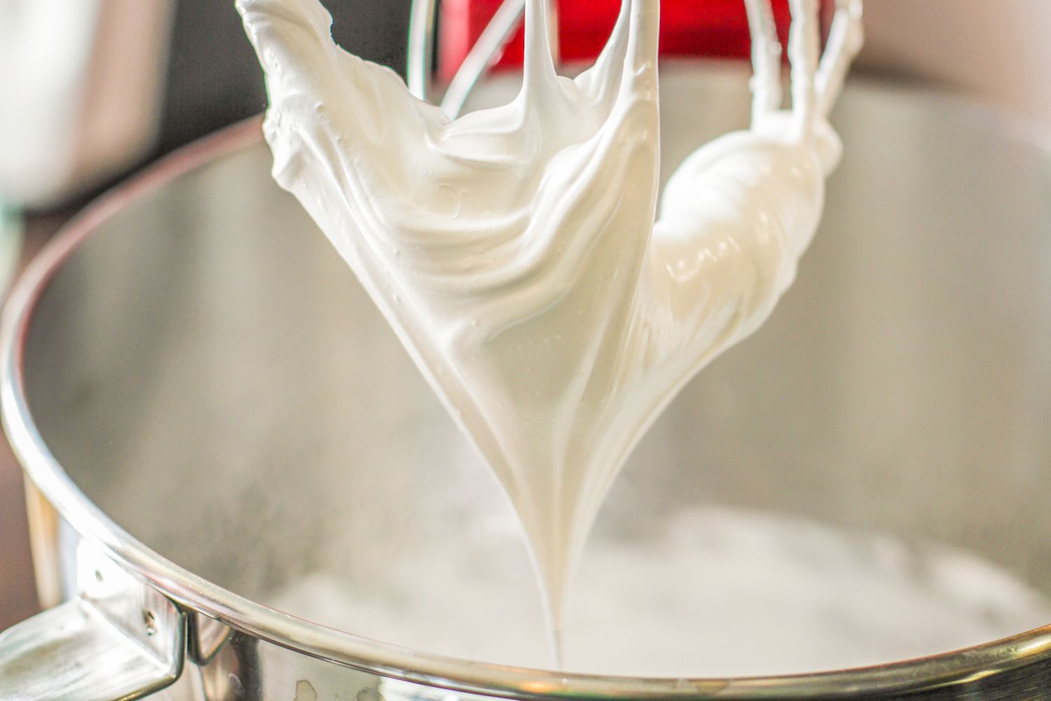 Whipped cream being prepared with a stand mixer, forming peaks in a metal mixing bowl