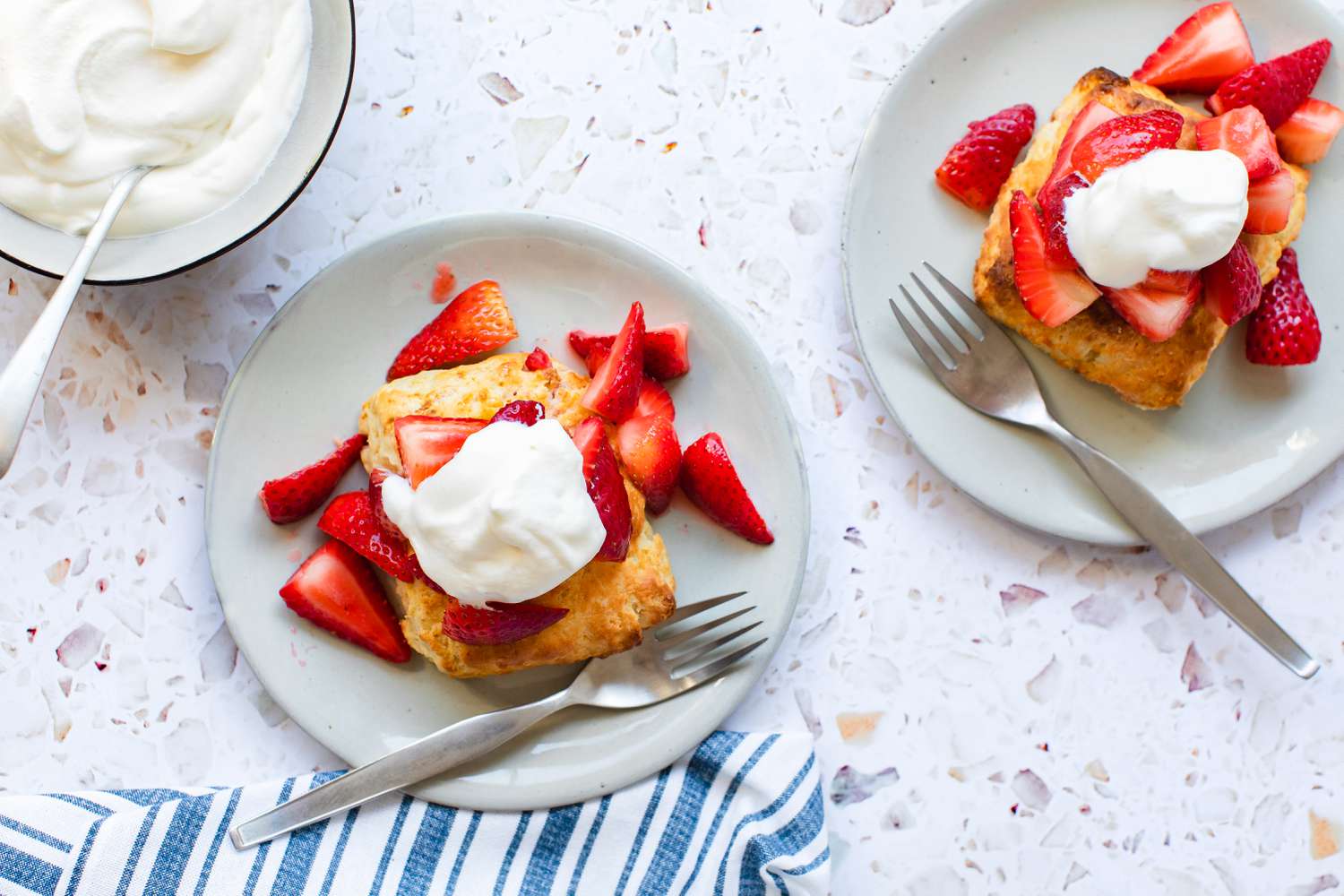 Two Plates of Easy Strawberry Shortcake with a Fork Next to a Bowl of Whipped Cream