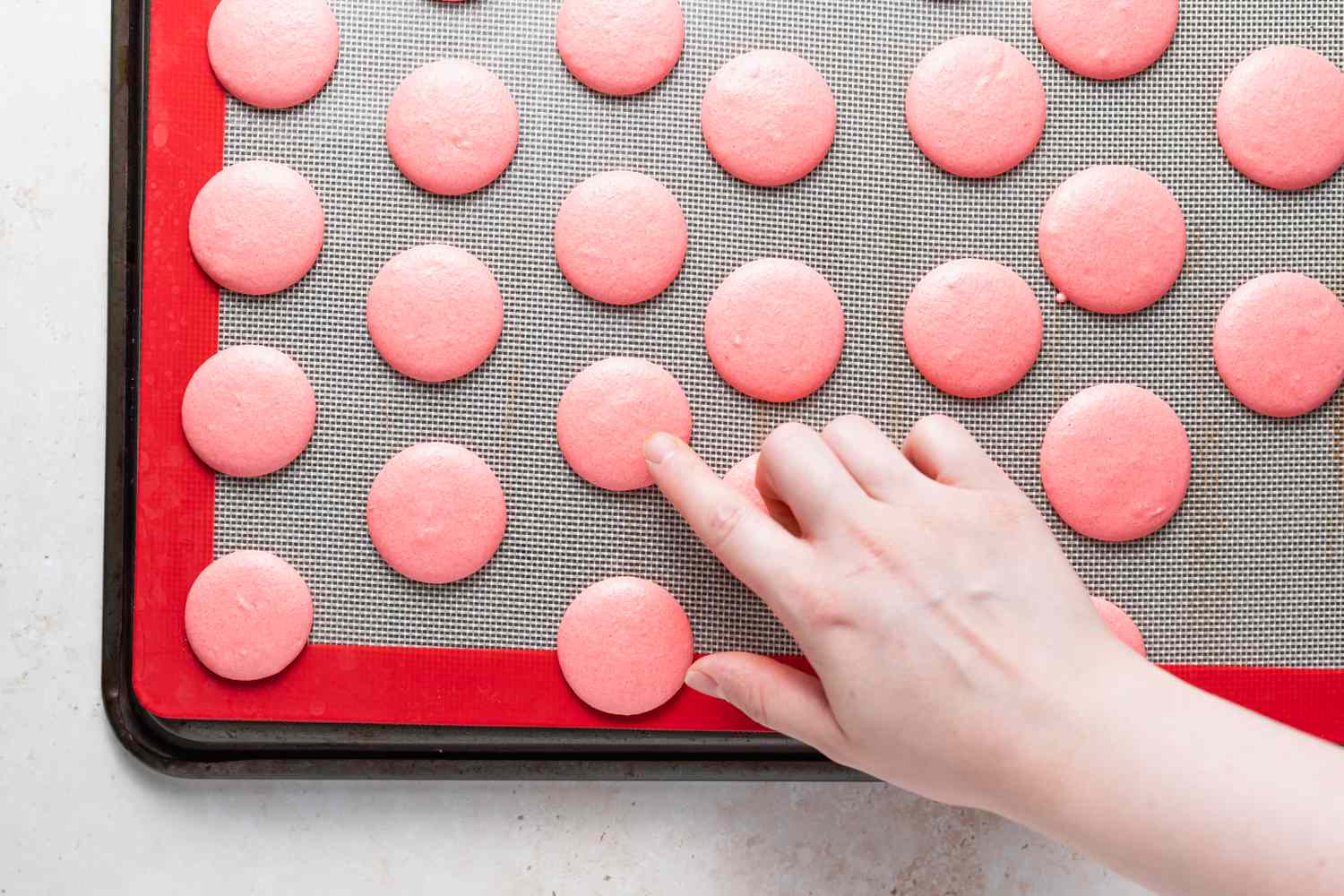 A finger touching piped macarons shells.