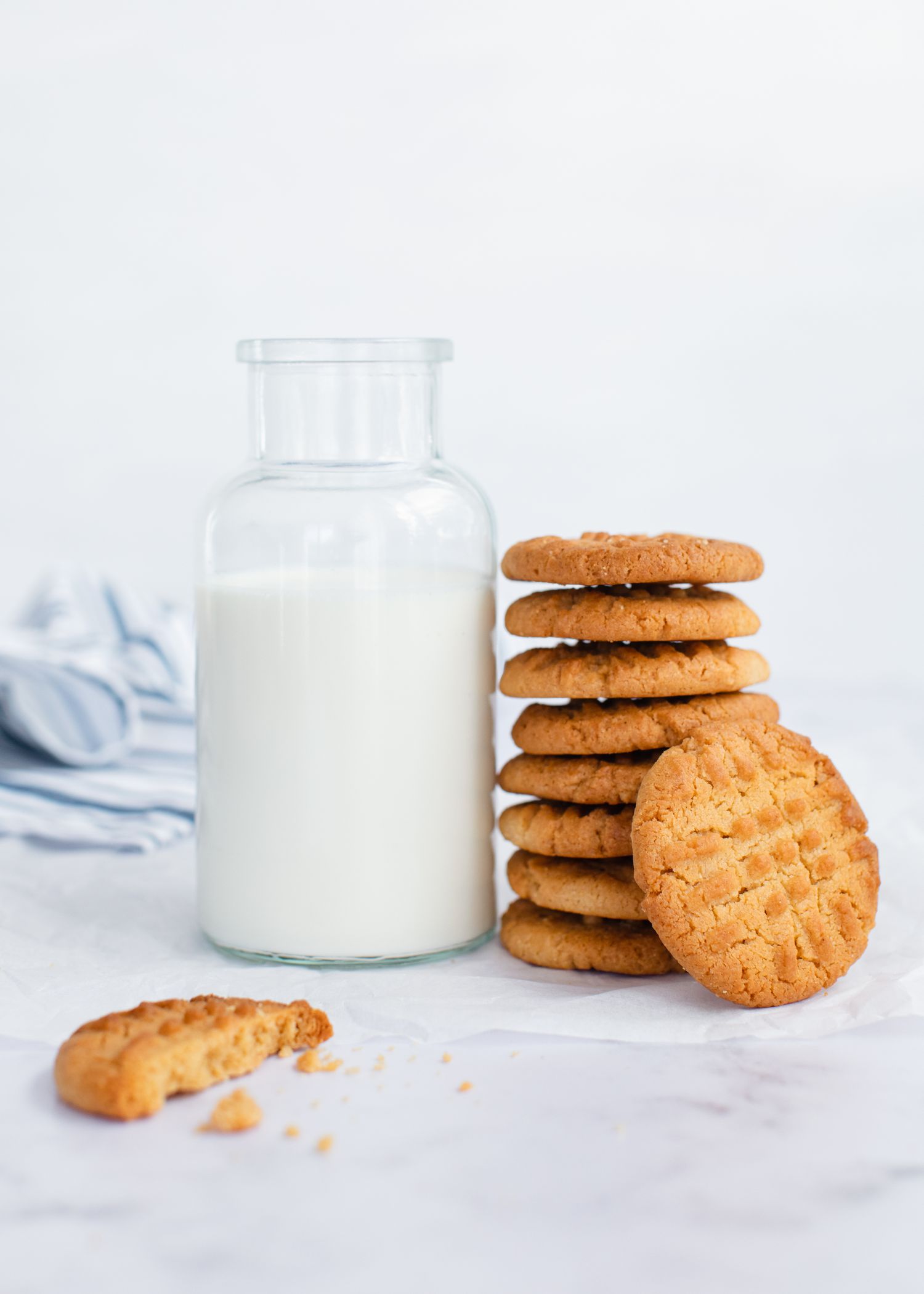 A stack of Peanut Butter Cookies next to a pitcher of milk.