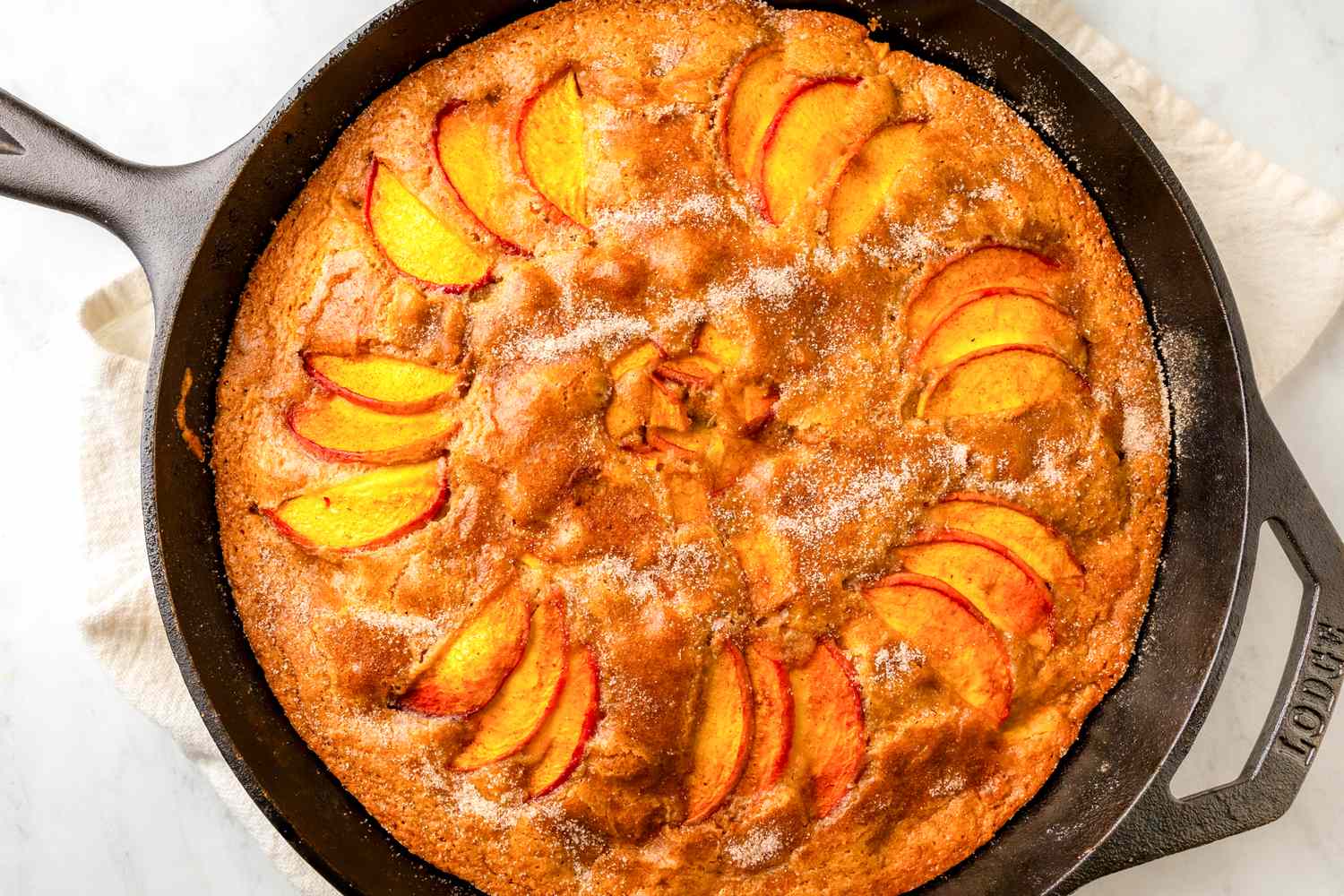 A peach cake baked in a cast iron skillet slices of peach arranged on top