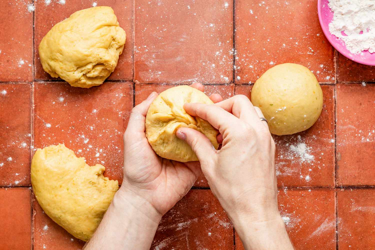 Hand pinching the bottom of a dough portion to form into a ball for pan de muerto recipe 