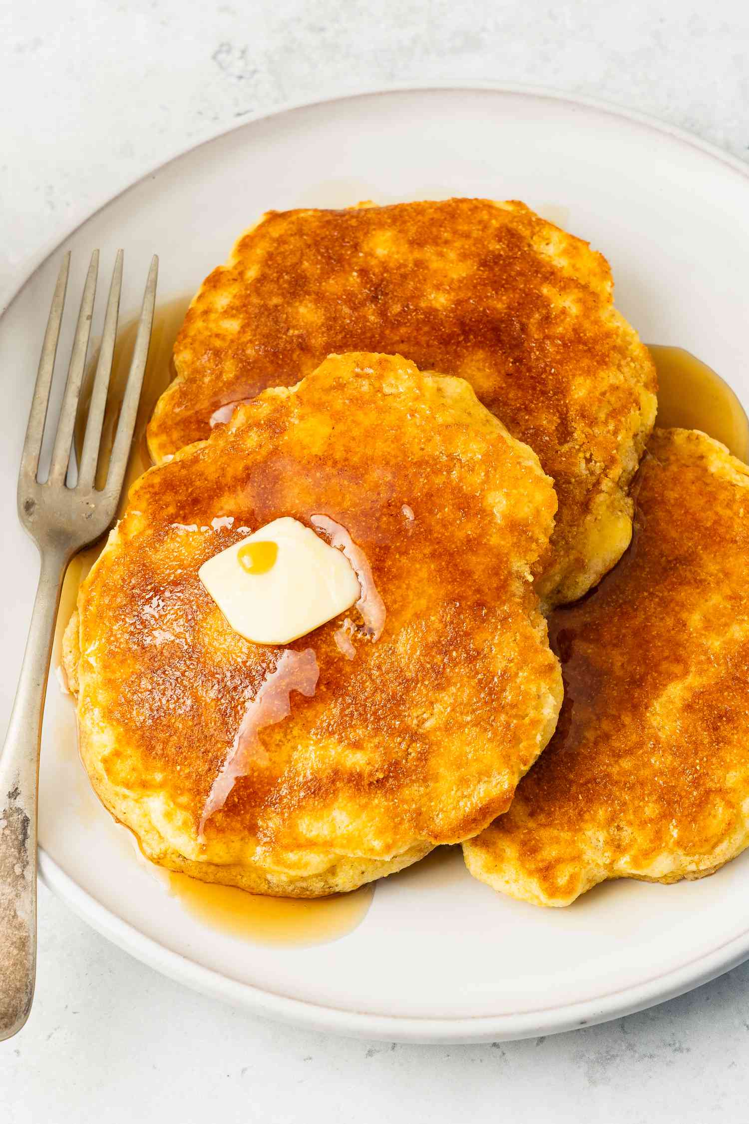 Jiffy corn mix pancakes topped with maple syrup and a slab of butter on a plate