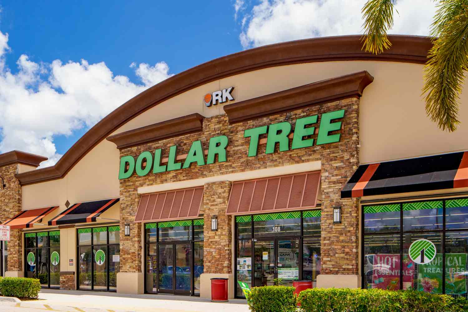 A Dollar Tree retail store with prominent signage surrounded by greenery and a sunny blue sky