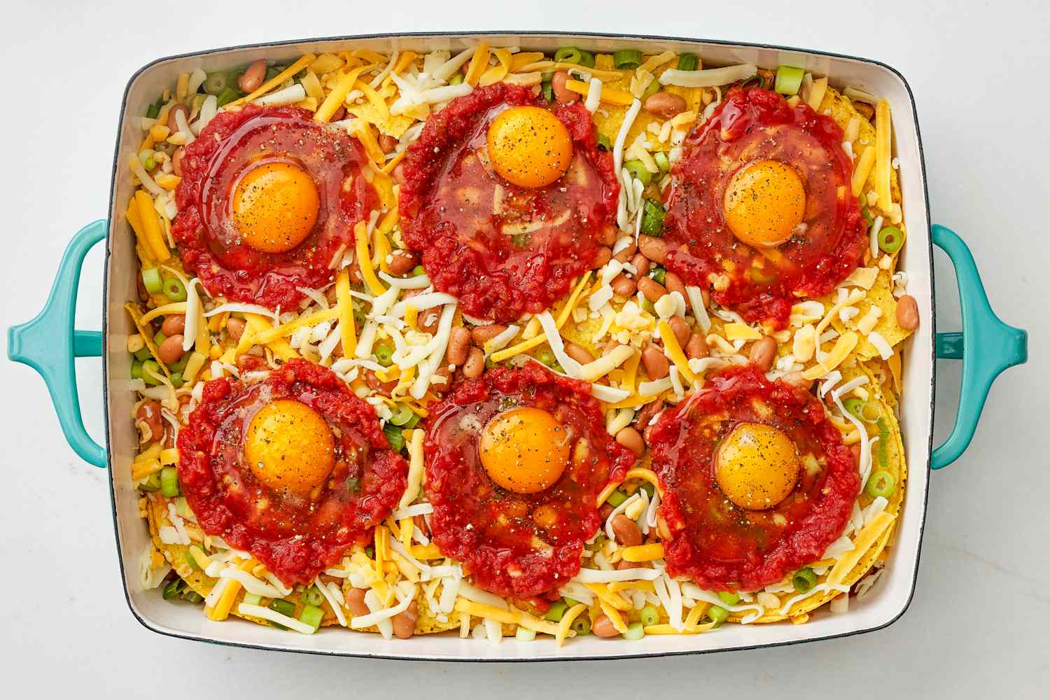 Wells of tomato sauce topped with an egg per well, all on top of huevos rancheros casserole in a casserole dish 