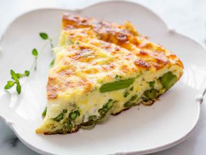 A slice of asparagus Frittata on a white scalloped plate