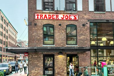 A brick building with a Trader Joes store people walking on a street outside