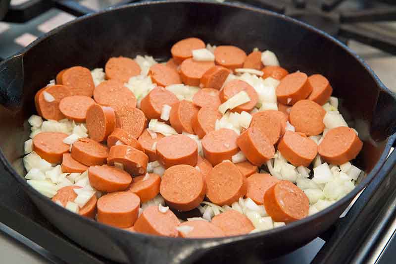 sautéing hot dogs in skillet with onion