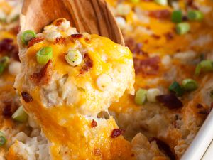 A wooden spoon lifting a serving of twice baked potato casserole from a baking dish
