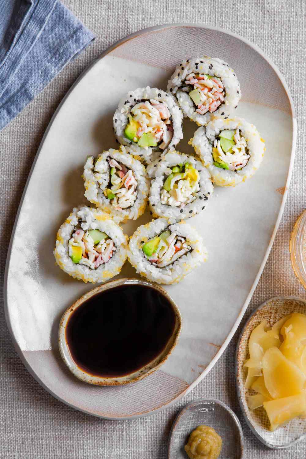 California Rolls on a Plate Next to a Small Bowl of Soy Sauce, Small Bowl of Pickled Ginger, and Small Saucer of Wasabi