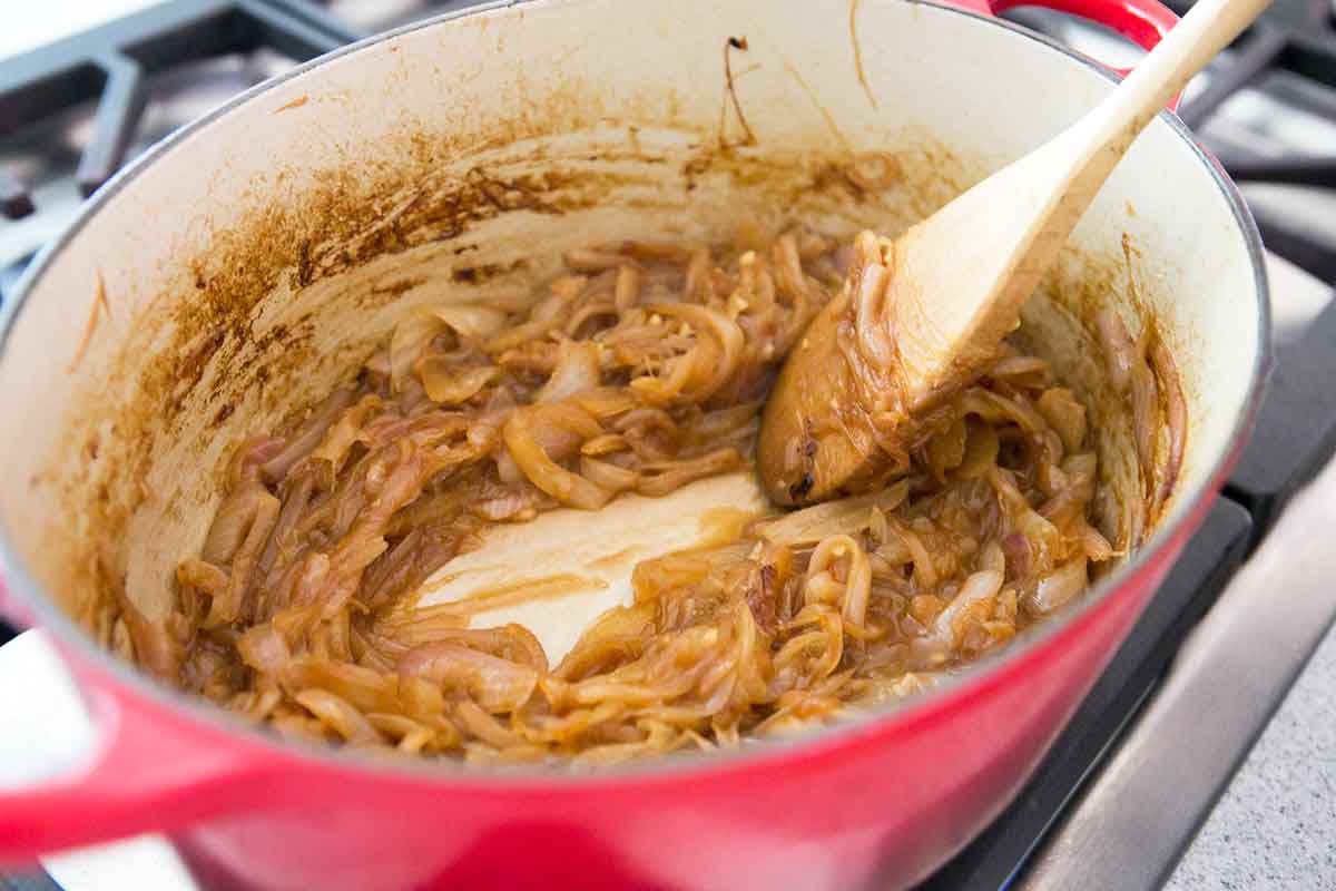 A wooden spoon stirring cooking onions in a large pot