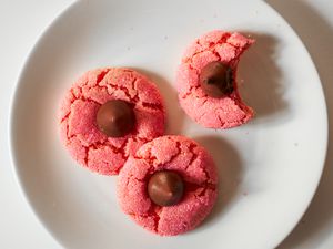 Overhead view of a white plate of three strawberry chocolate kiss cookies on a white background
