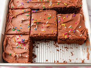 A chocolate cake in a rectangular baking pan with chocolate frosting and colorful sprinkles partially cut into squares