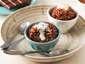 Bowls of chocolate rice dessert topped with cream on a large plate with spoons