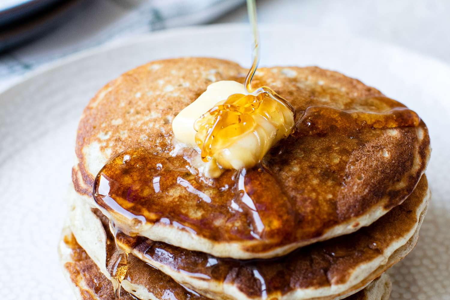 Stack of Buckwheat Pancakes Topped with Maple Syrup and Some Butter, and Next to It, a Glass of Milk and a Container of More Syrup