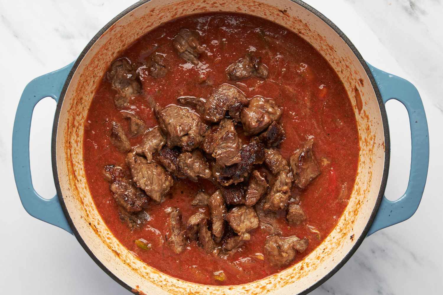 Cooked chuck roast added to the sauce in the Dutch oven for carne picada recipe