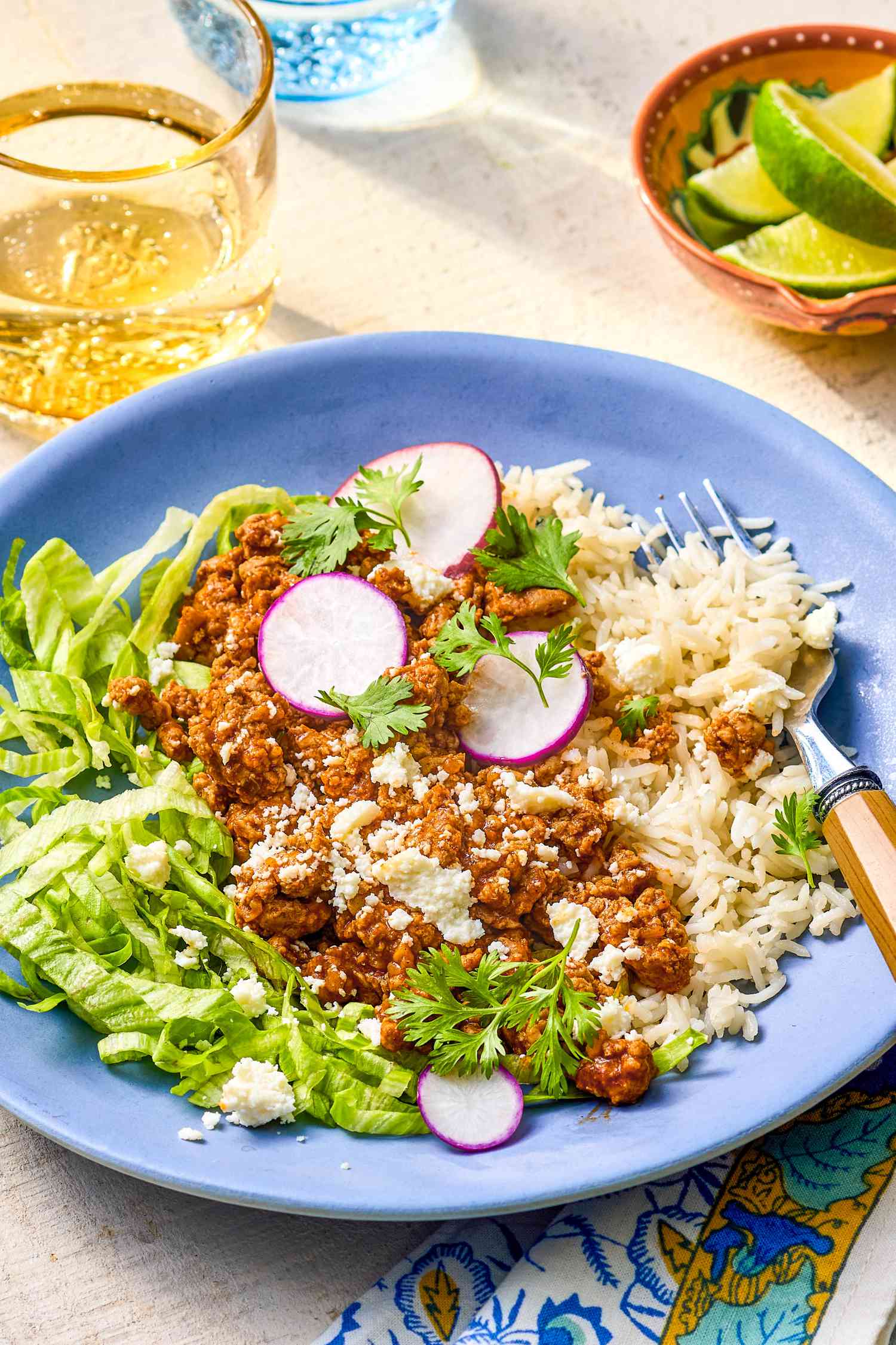 Plate of 5-ingredient turkey taco bowl at a table setting with a glass of water and a bowl of lime wedges