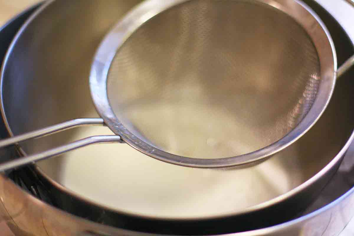 mesh strainer over the bowl of eggnog cream