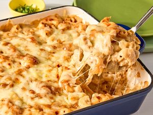 A casserole dish with cooked French onion mac and cheese some being lifted out with a serving utensil