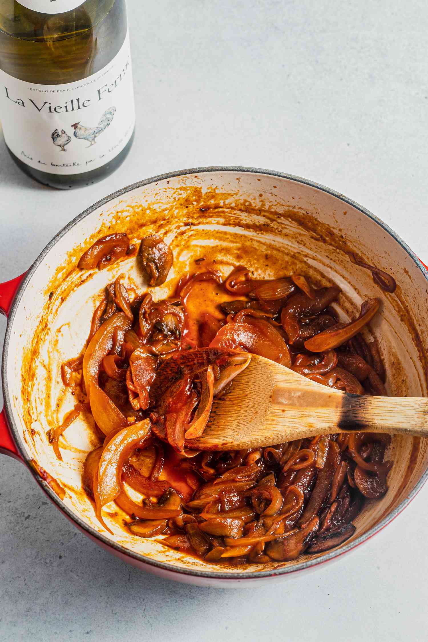 Dutch Oven with Caramelized Onions Mixed with a Wooden Spoon, and Next to It, a Bottle of White Wine for How to Deglaze a Pan