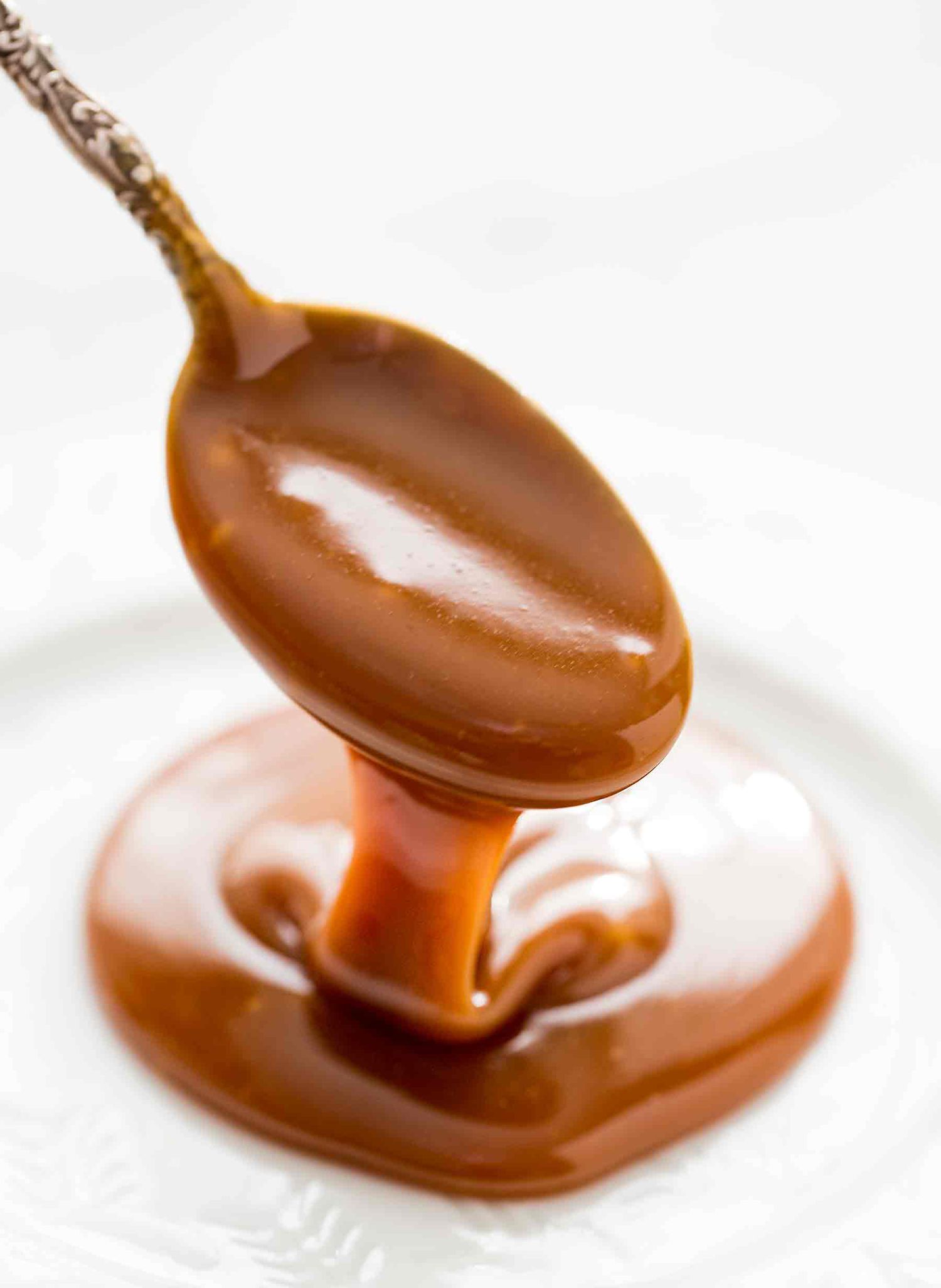 A spoon drizzling thick caramel sauce onto a plate
