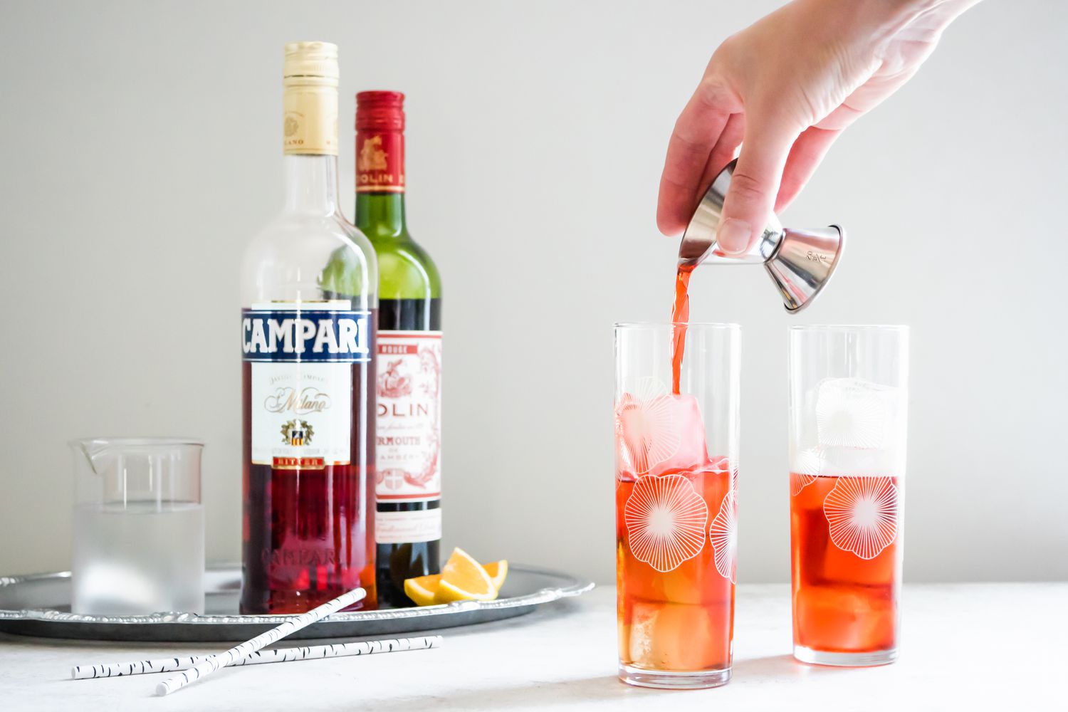 Compari Poured into Two Glasses for Americano Cocktail with the Rest of the Ingredients in the Background