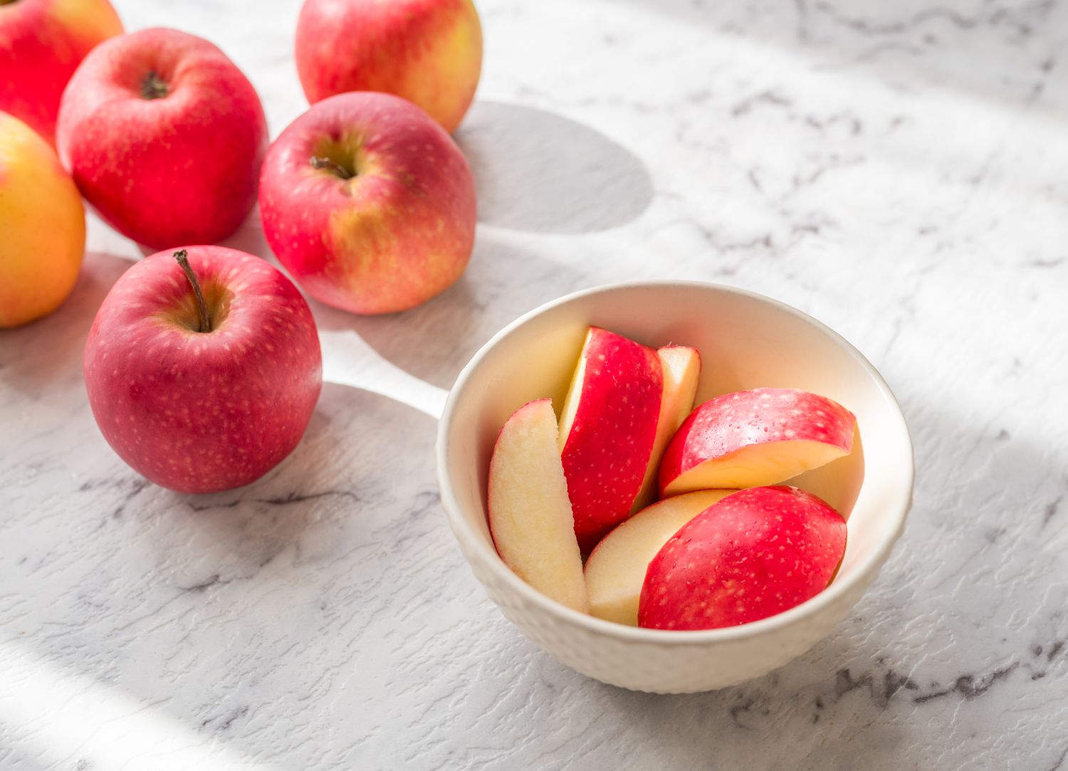 bowl of sliced apples on a counter near a couple of uncut apples