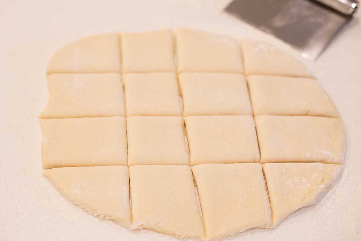 The dough for overnight beignets are rolled and cut. A bench scraper is in the right upper corner.
