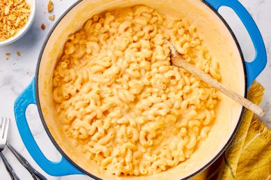 One pot mac and cheese in a dutch oven with a wooden spoon, and in the surroundings, a bowl with cracker topping and a mustard kitchen towel