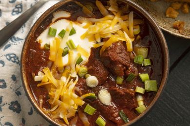 A bowl of chili with shredded cheese sour cream and green onions