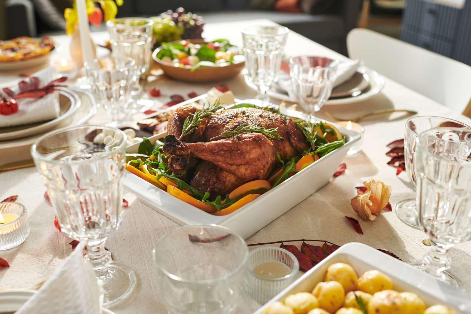 A roasted turkey served at a dinner table set with plates glasses and side dishes for Thanksgiving