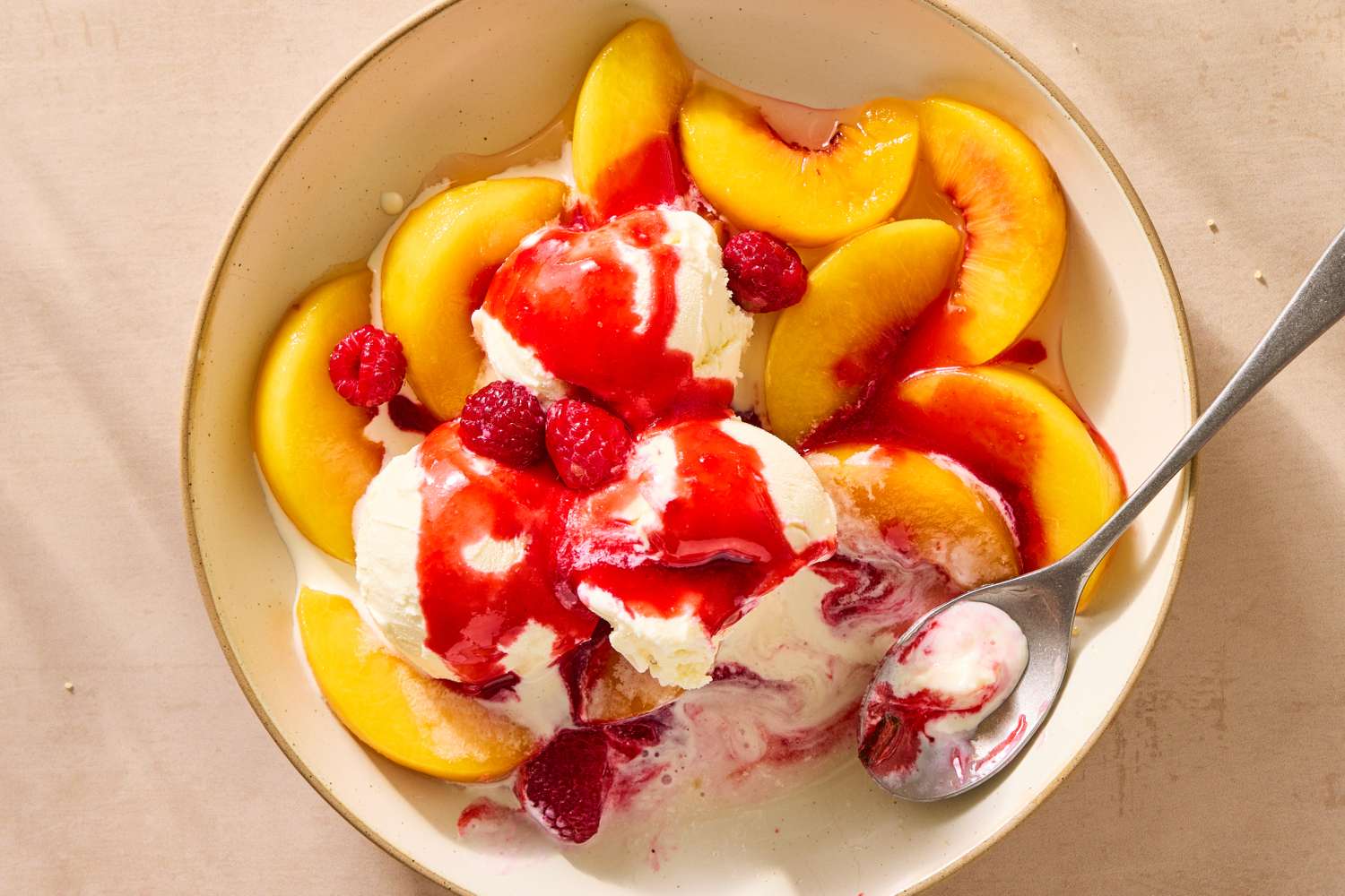 Bowl with sliced peaches, scoops of ice cream, raspberries, and red sauce