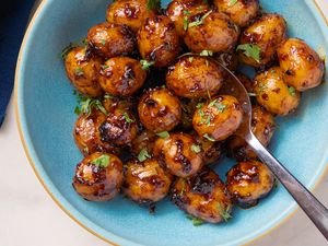 A bowl of Southwestern sticky potatoes coated in a saucy glaze with chopped herbs served with a spoon