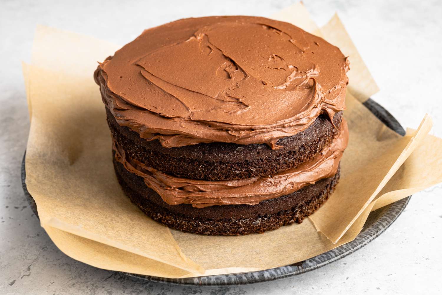 Layers of One-Bowl Double-Layer Chocolate Cake on the Parchment Covered Plate With Icing Between the Layers and on the Top Layer 