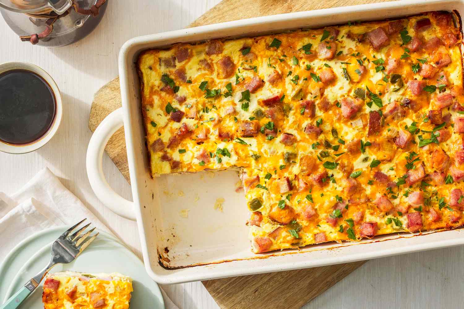 Denver omelette hashbrown casserole in a casserole dish at a table setting with a serving on a plate, a cup of coffee, and a jar