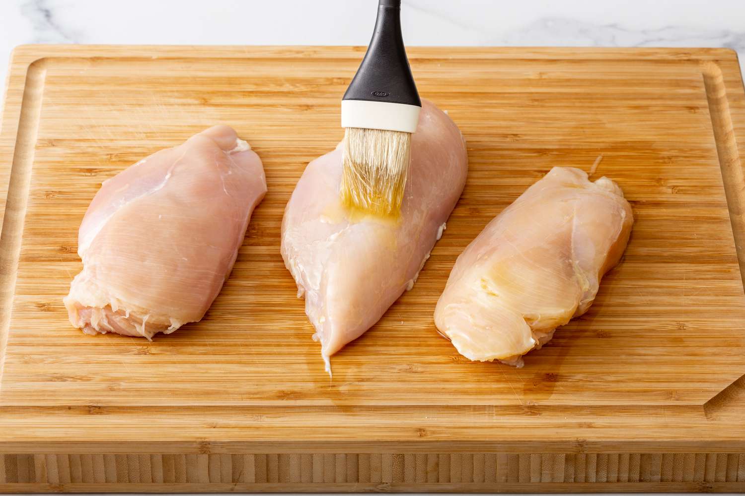 Chicken breasts being brushed with oil on a cutting board to show how to cook chicken breast.
