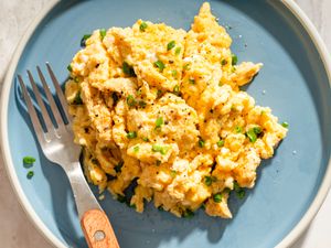 A plate of scrambled eggs garnished with herbs served with a fork
