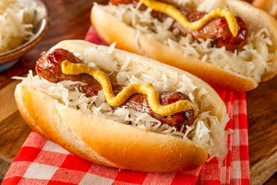 Two bratwurst sausages served in buns topped with mustard and sauerkraut on a checkered tablecloth