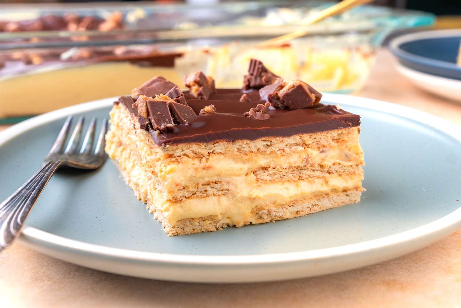 Side view of cake on a blue plate with a fork. Extra plates and the cake pan are visible in the background